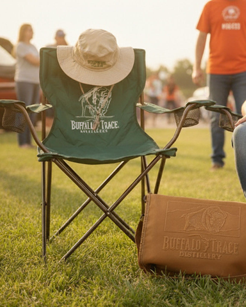 Green folding chair and brown leather bag with 'Buffalo Trace' logo on grassy field.