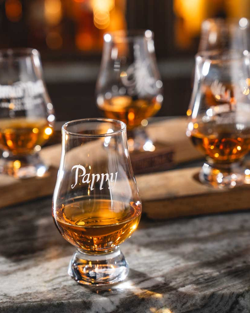 Four glencairns of Pappy Van Winkle's whiskey on a wooden board with a blurred background.