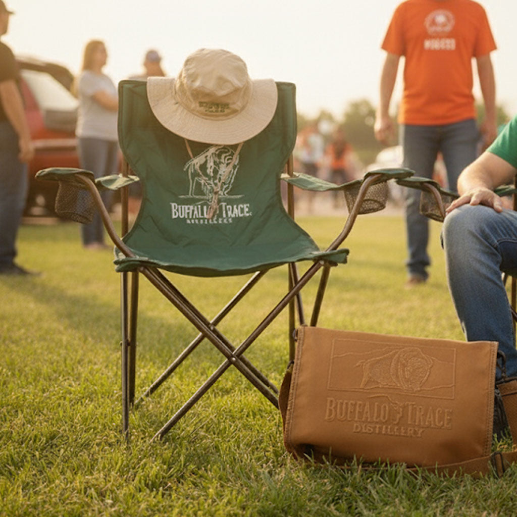 Green folding chair and brown leather bag with 'Buffalo Trace' logo on grassy field.