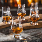 Four glencairns of Pappy Van Winkle's whiskey on a wooden board with a blurred background.